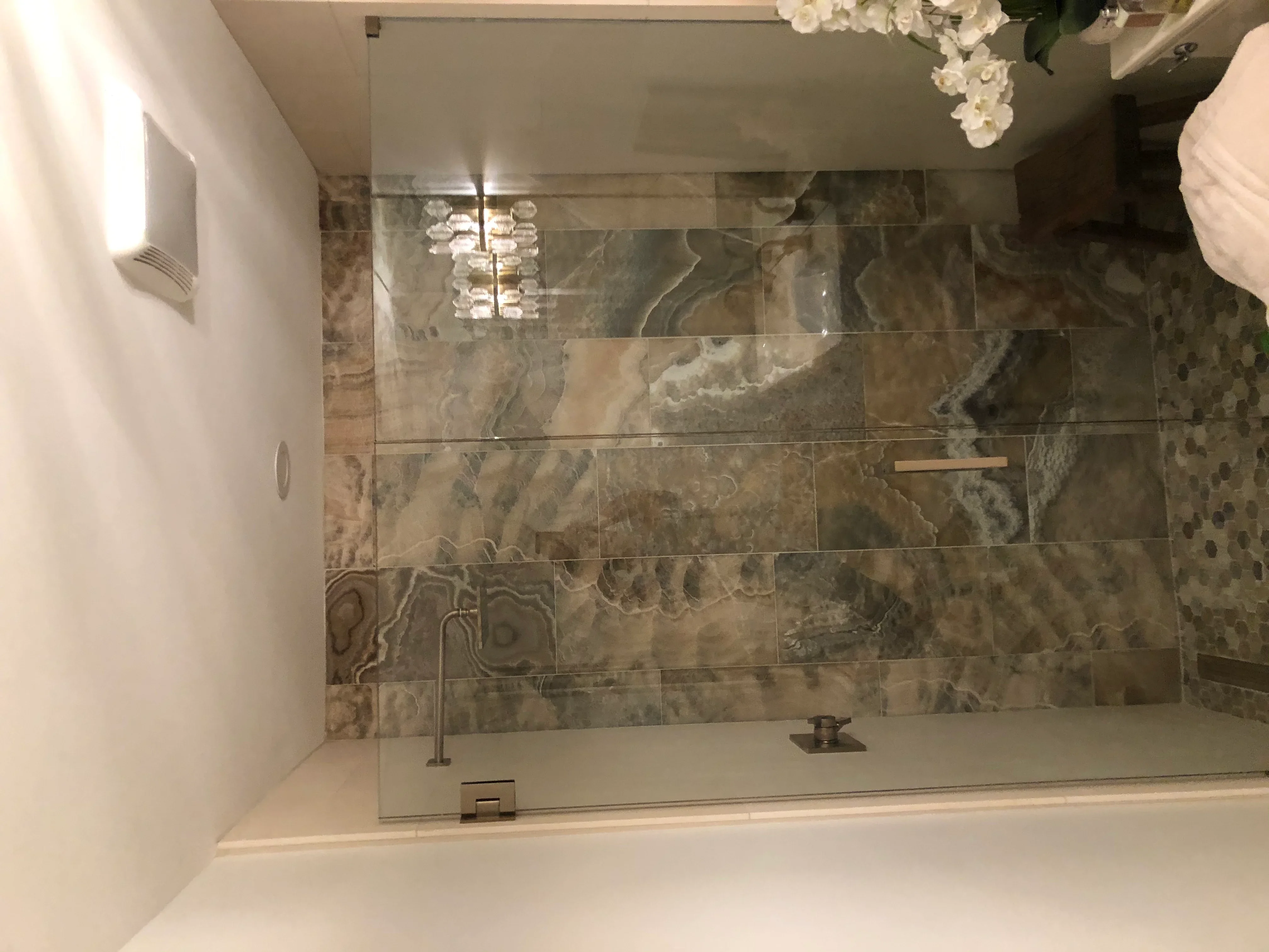 Frameless glass shower with natural stone tile surround and chrome fixtures in luxury bathroom
