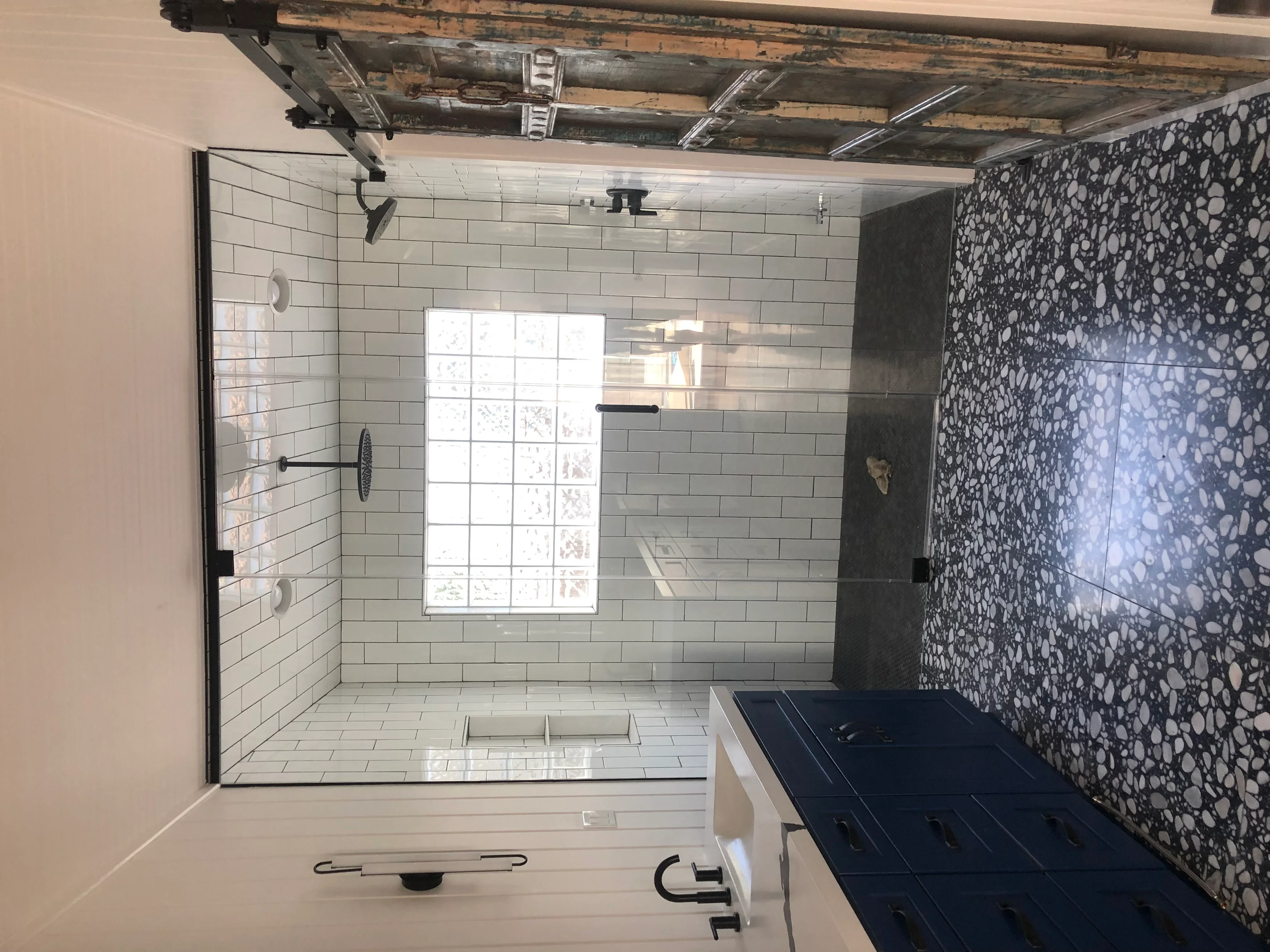 Modern bathroom with white subway tile, frameless glass shower, and dark terrazzo accent wall
