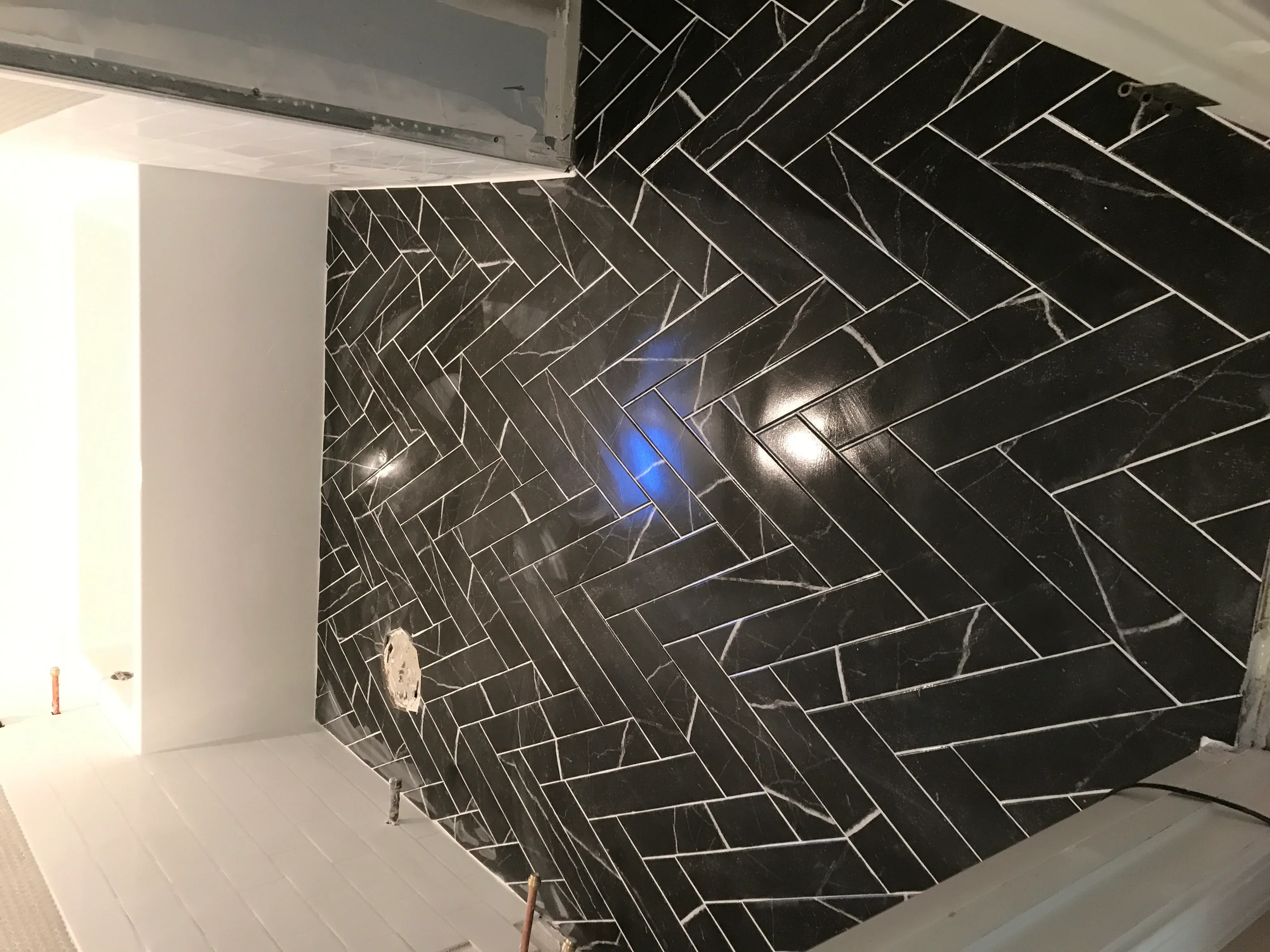 Black herringbone tile wall with white grout lines and recessed lighting in bathroom