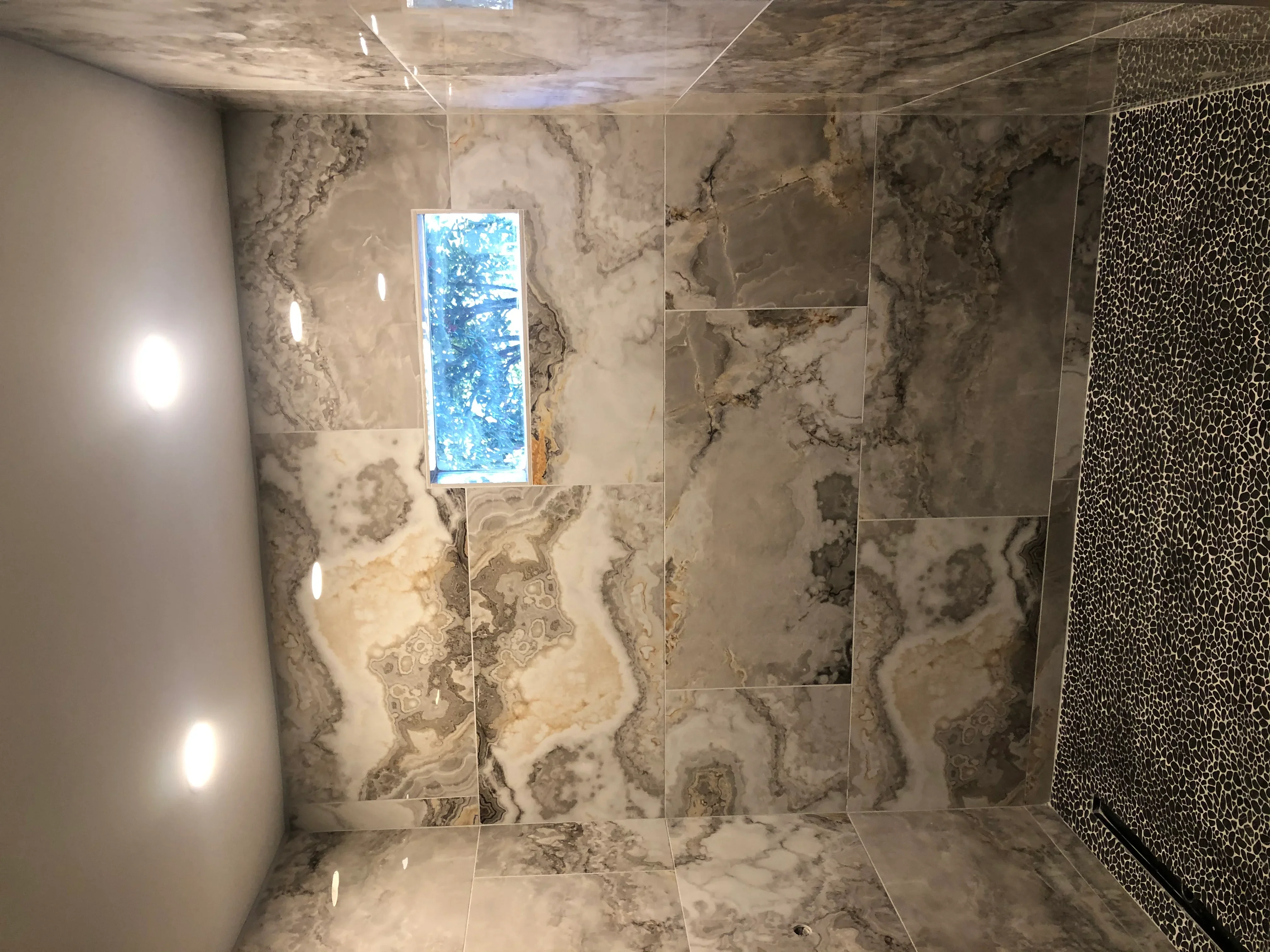 Marble shower with veined tile walls, mosaic accent panel, and frameless glass enclosure