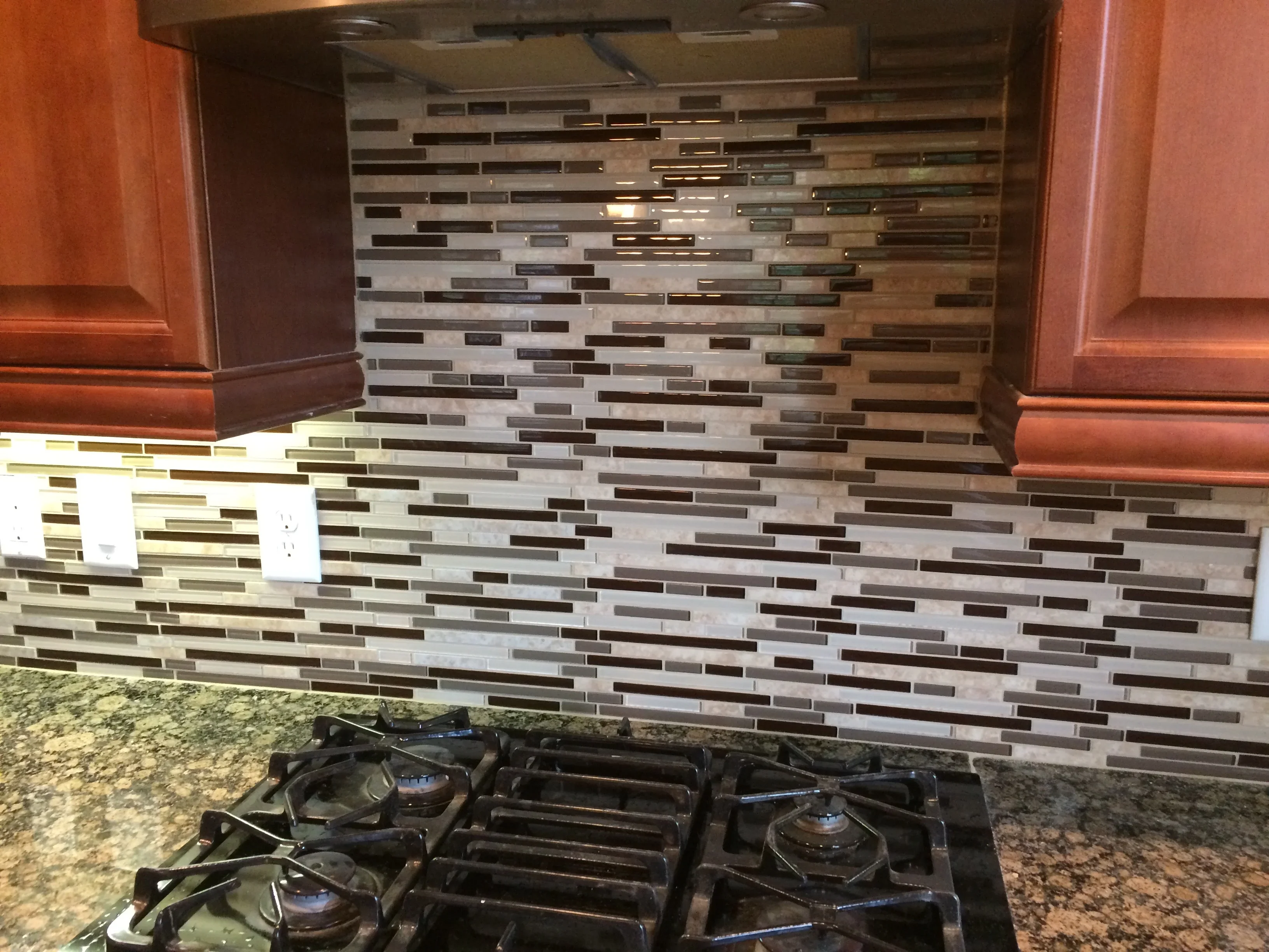 Modern linear glass and stone backsplash with staggered pattern above gas cooktop