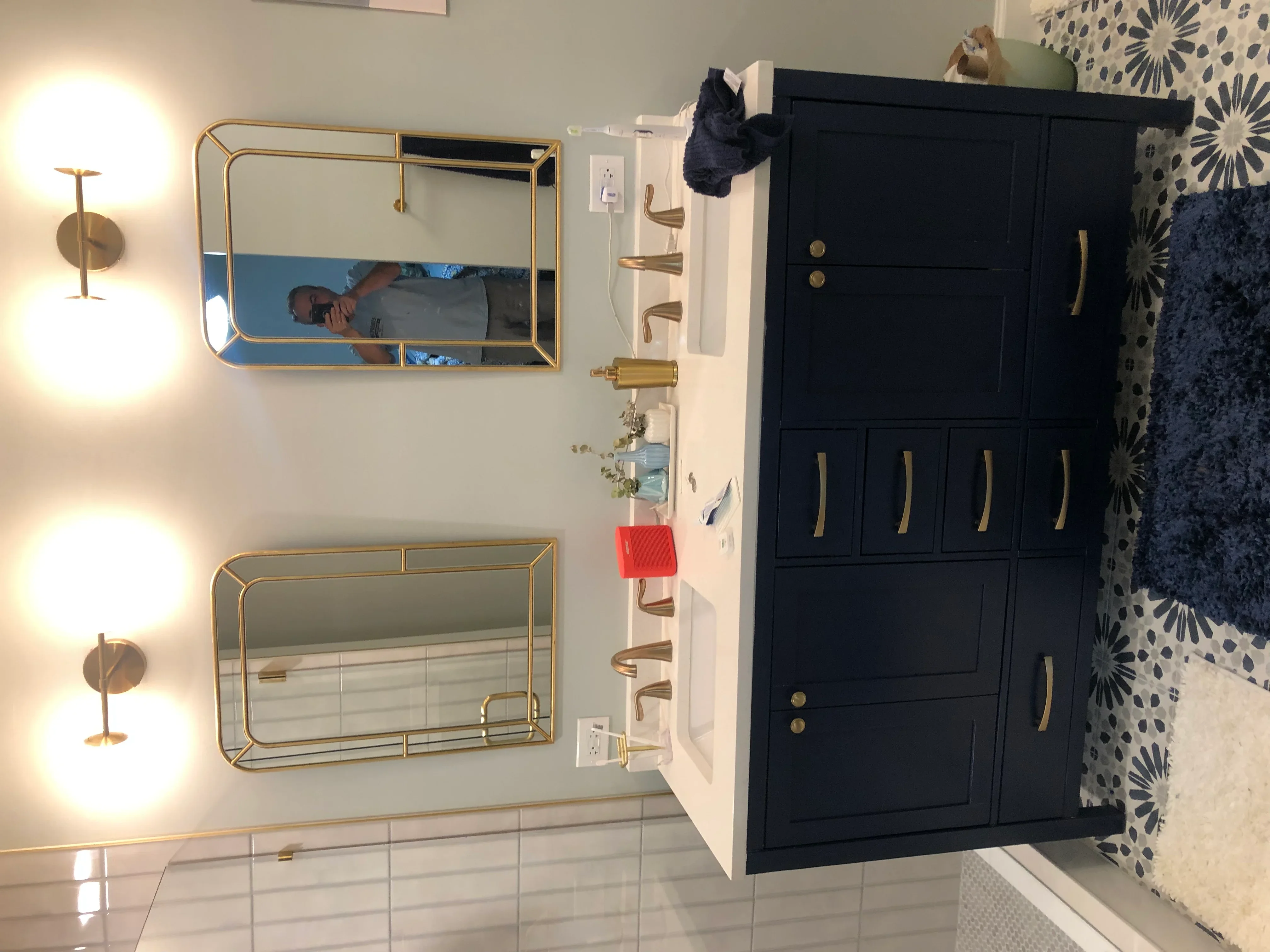 Modern bathroom with navy vanity, brass mirrors, and dual wall sconces