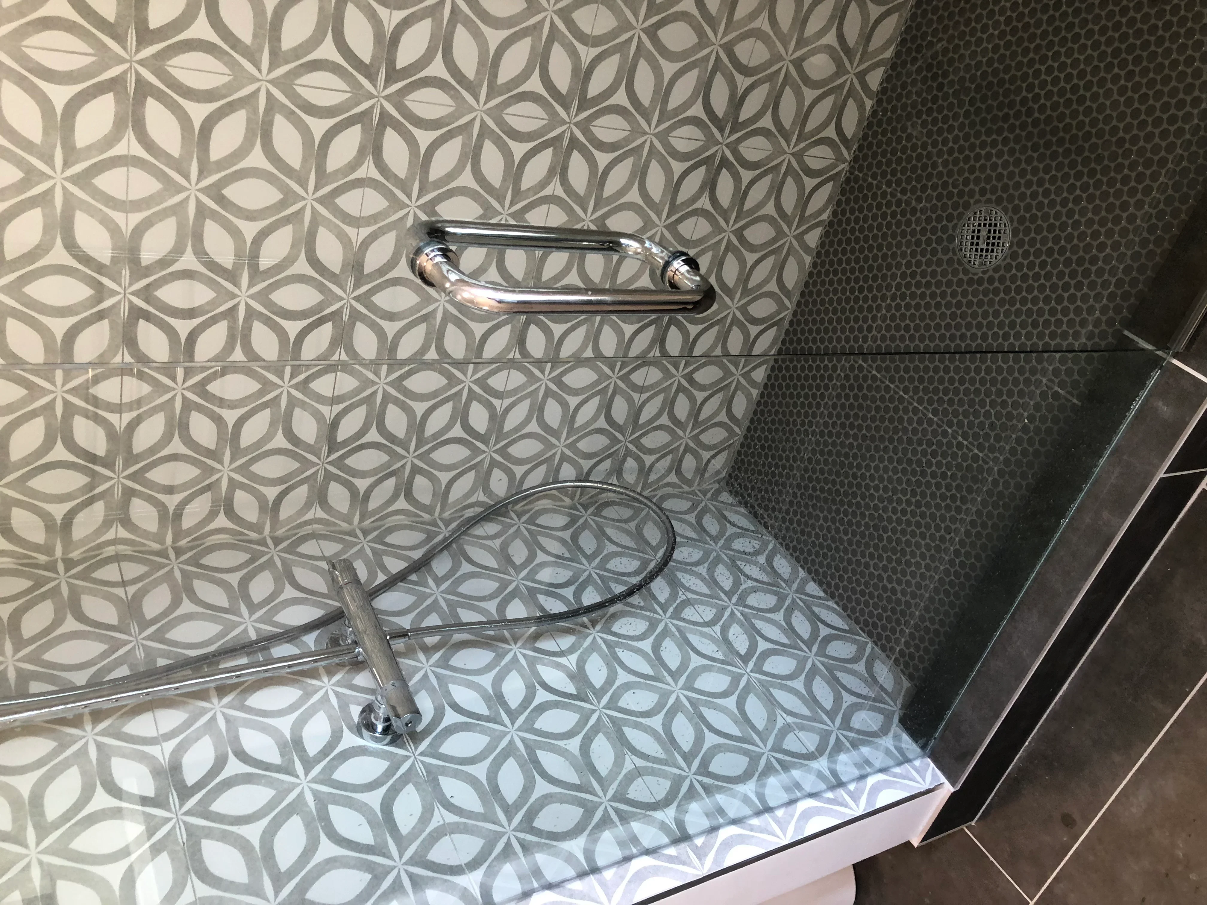Modern shower with geometric patterned walls and dark hexagonal floor tile, chrome grab bar and fixtures