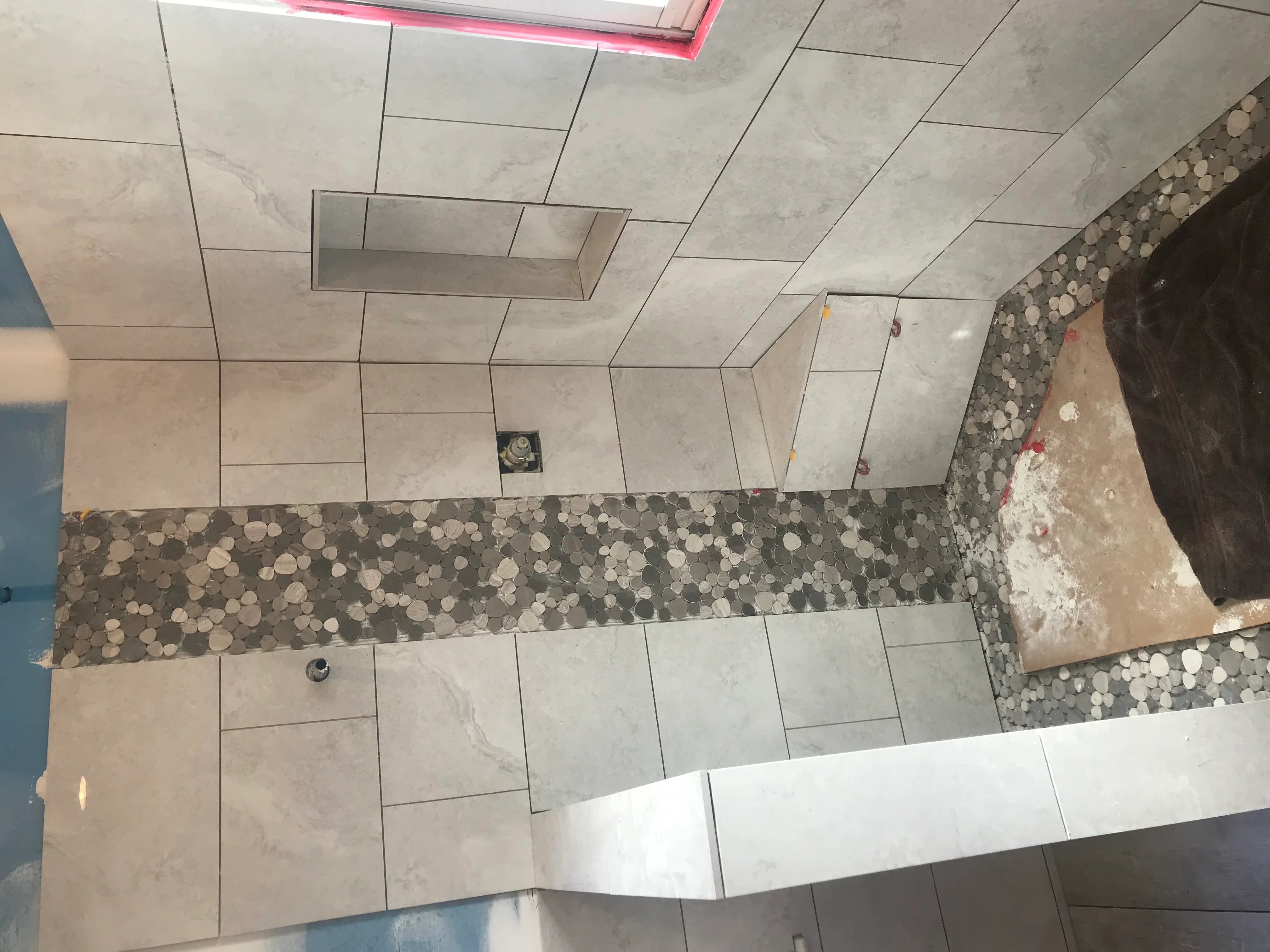 Bathroom tile installation with large porcelain tiles and decorative penny tile accent strip