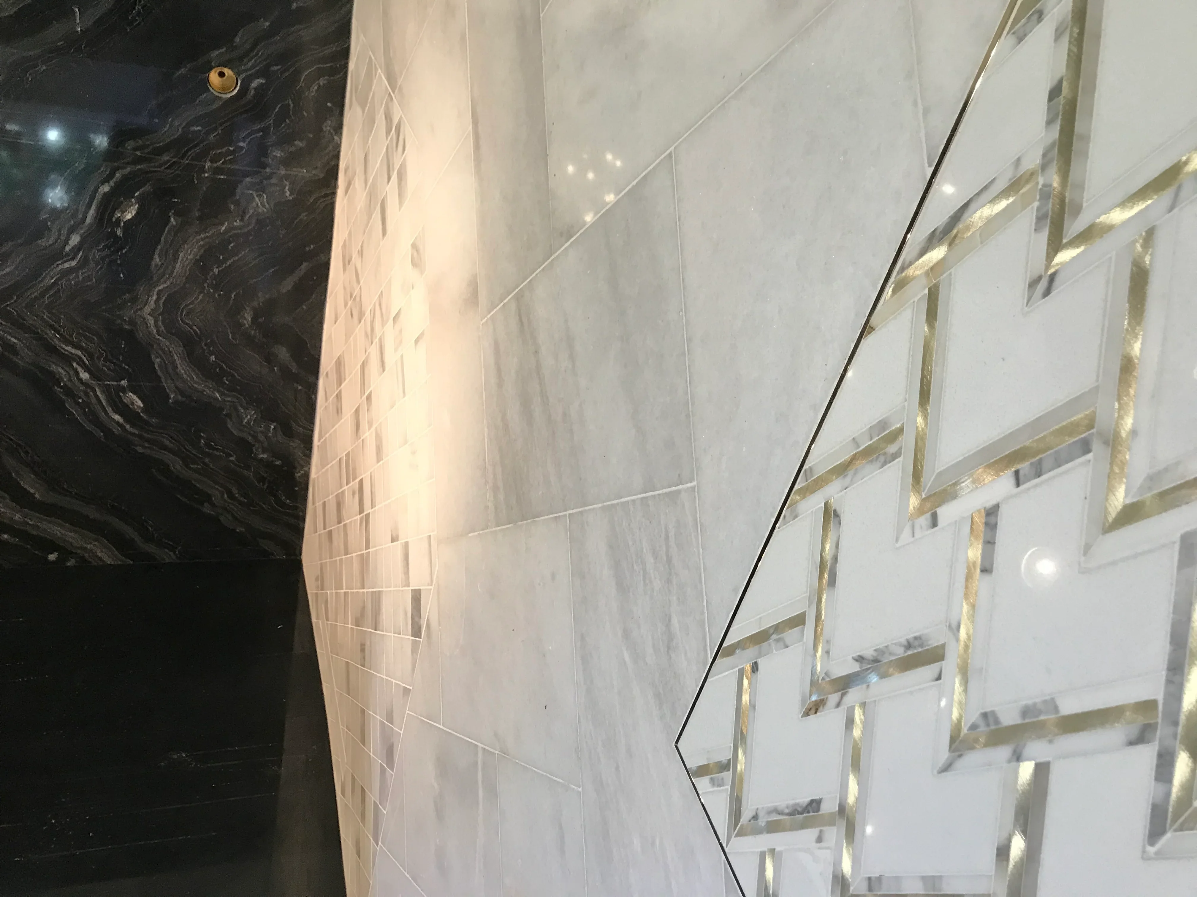 Black marble accent wall with light gray marble floor tiles and brass-framed glass shower enclosure
