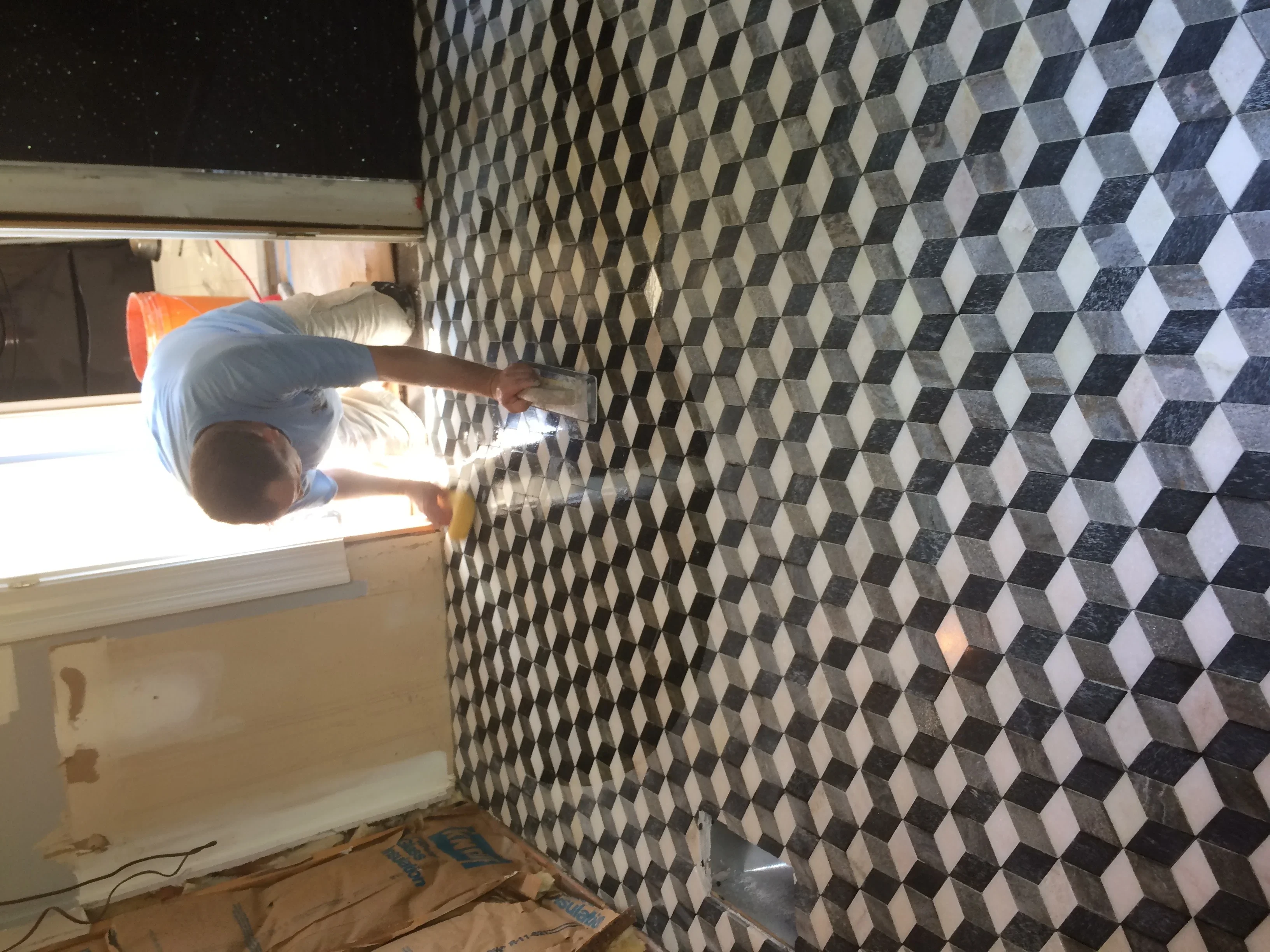 Worker installing black and white 3D diamond pattern tiles on bathroom wall