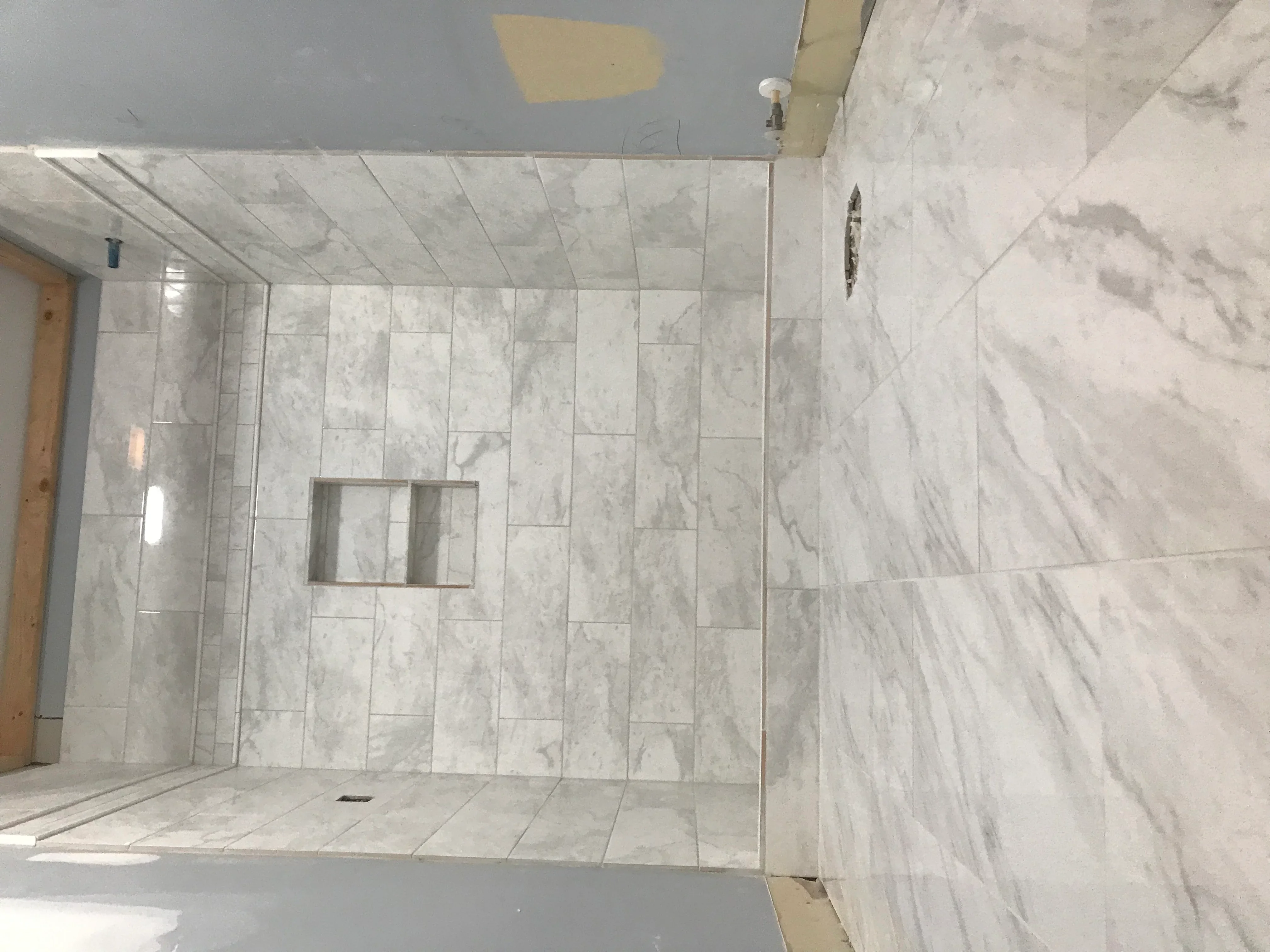 Marble tile shower with linear pattern, recessed niche, and frameless glass door